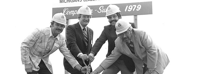 black and white photo of 4 white men holding a shovel with a sign behind them