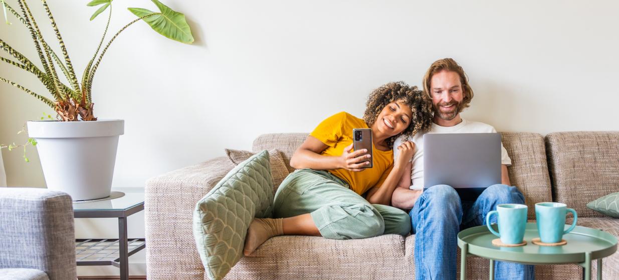 Multiracial young couple using computer laptop and smart mobile phone sitting on the sofa at home