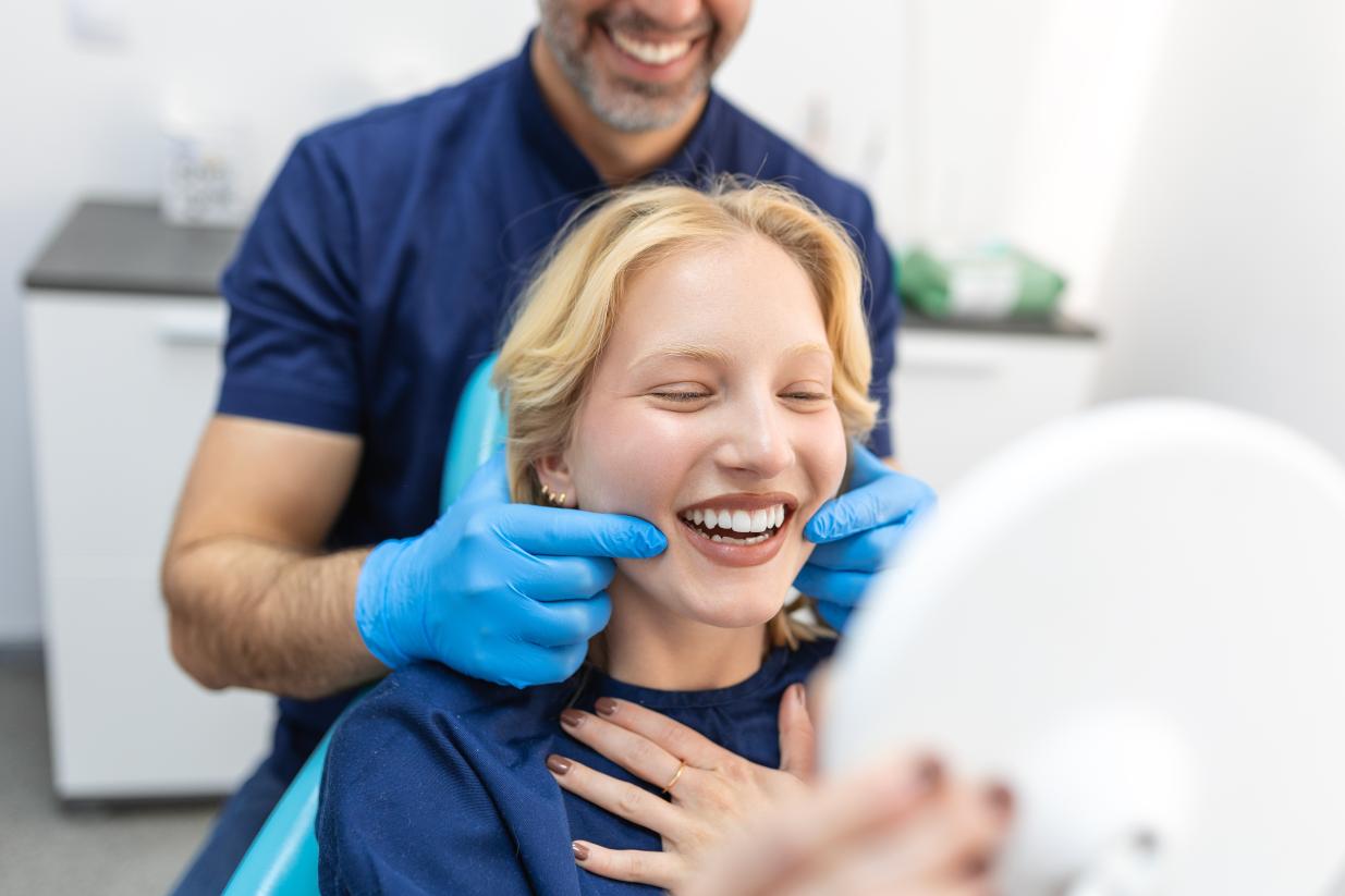 Patient in a dentist chair smiling in a mirror while the dentist is pointing at her teeth