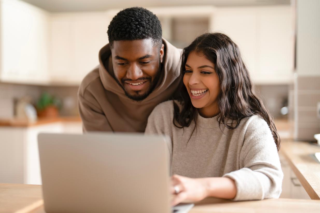 A male and female couple looking at a laptop together smiling
