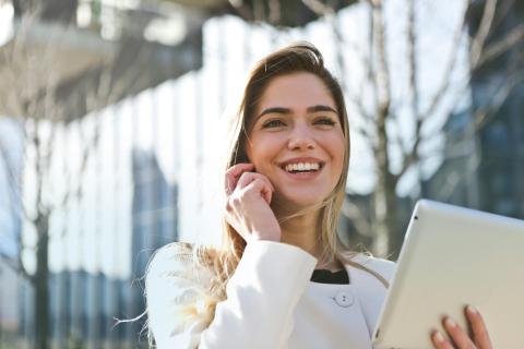 A woman talking on the cellphone in front of a building and smiling