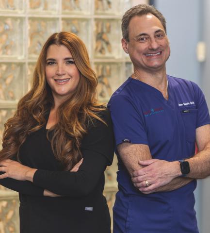 A male and female dentist standing back to back smiling in an office