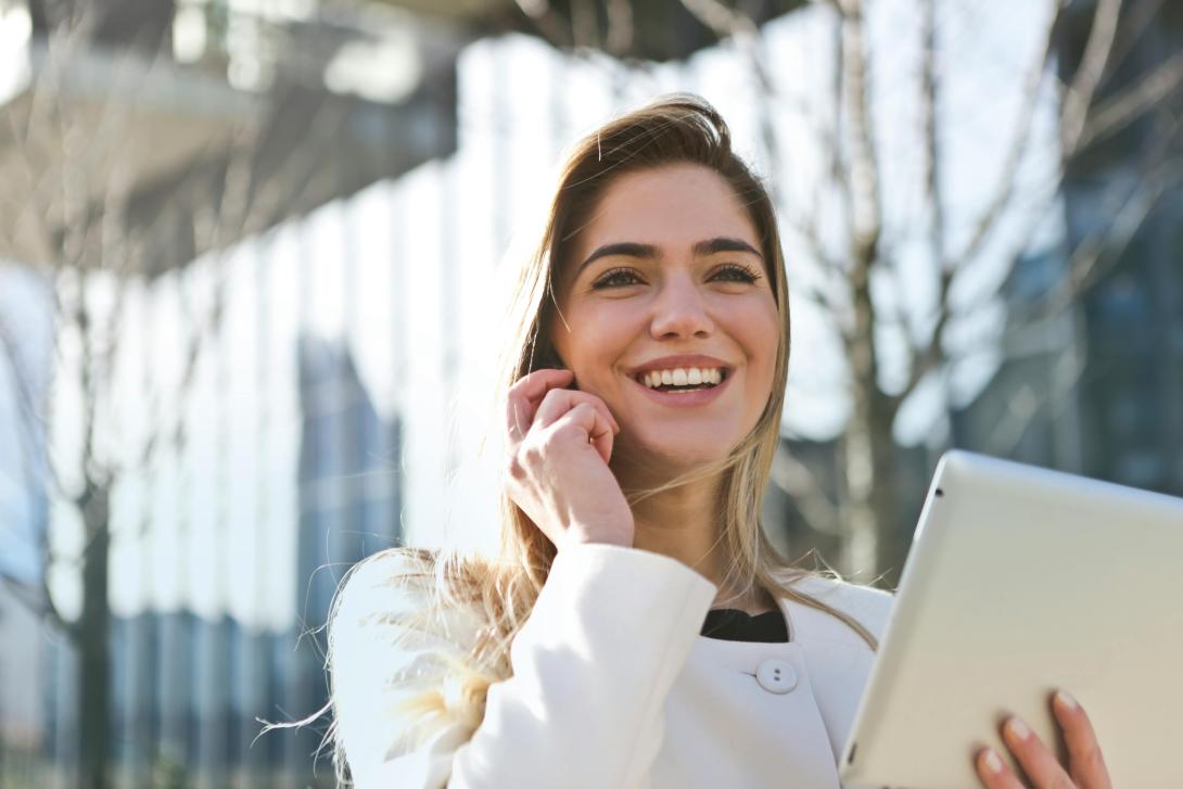 A woman talking on the cellphone in front of a building and smiling