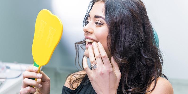 a smiling woman looks into a yellow hand mirror