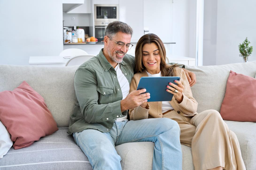 A male and female couple sitting on a couch looking at a tablet together